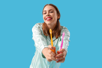 Beautiful young woman with toothbrushes on blue background