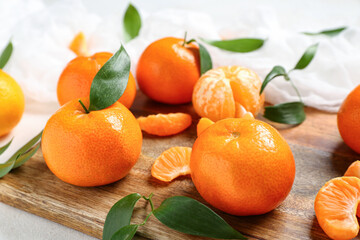 Wooden board with sweet mandarins and leaves on white background
