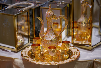 Eastern pitcher stand on a tray and copper glasses on blurred background, close up. East Tableware. Arabic, Turkish tea served in a golden teapot, carafe. Arabian jugs and glasses selective focus