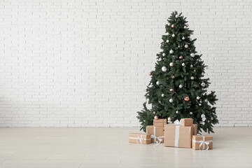 Beautiful Christmas tree with gift boxes near white brick wall