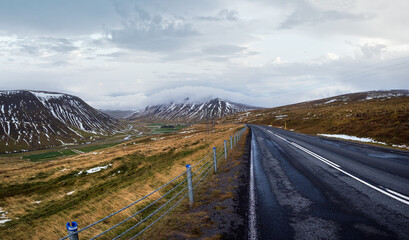 Highway road and mountain view during auto trip in Iceland. Spectacular Icelandic landscape with  scenic nature: highland mountains, fields, clouds, glaciers, waterfalls.