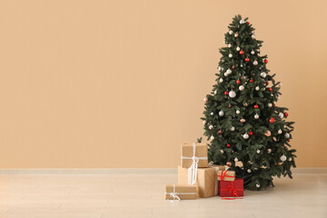 Beautiful Christmas tree with gift boxes near beige wall