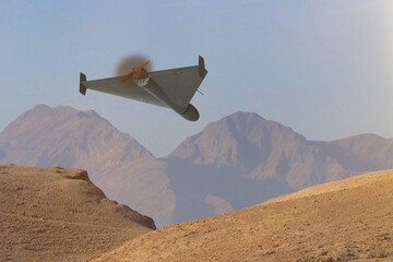 A military kamikaze drone flies over mountains in the desert against a backdrop of sky and clouds,...