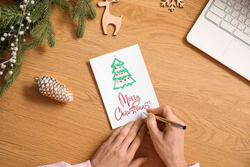 Mature woman writing greeting card for Christmas celebration on wooden table, top view
