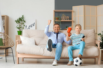 Mature doctor and his little son with soda watching football game at home