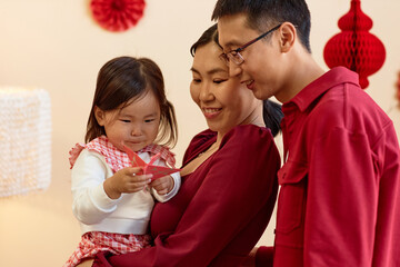 Portrait of happy Asian family with baby girl holding paper crane while decorating home for Chinese New Year together