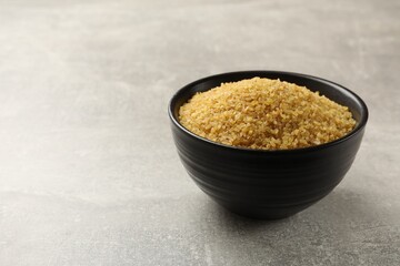Bowl with raw bulgur on gray table, space for text