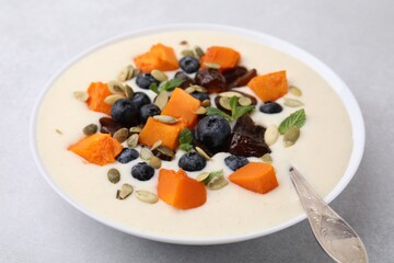 Delicious semolina pudding with blueberries, dates, pumpkin, mint and spoon in bowl on white table, closeup