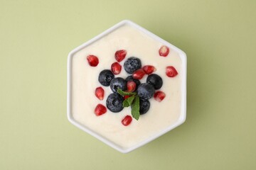 Bowl of delicious semolina pudding with blueberries, pomegranate and mint on light green background, top view