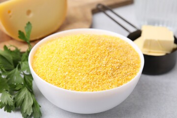 Raw cornmeal in bowl, parsley, cheese and butter on light table, closeup