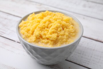 Tasty cornmeal in bowl on white wooden table, closeup