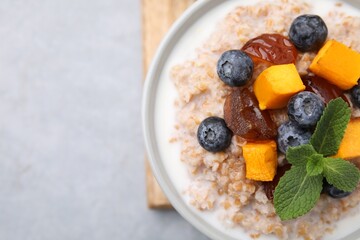 Tasty wheat porridge with pumpkin, dates and blueberries in bowl on light gray table, top view. Space for text
