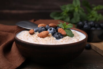 Tasty wheat porridge with milk, blueberries and almonds in bowl on wooden table, closeup