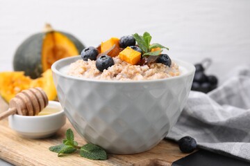 Tasty wheat porridge with pumpkin, dates and blueberries in bowl on table, closeup