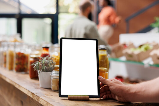 Close-up of electronic tablet displaying blank chromakey mockup template. Detailed image of digital device showing an isolated white screen in eco friendly bio food store.