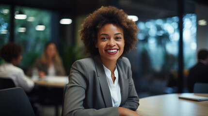 Fototapeta premium Portrait of a businesswoman. Beautiful black African American woman smiling wearing formal outfit suit in office sitting at desk.