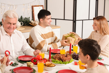 Happy young couple with Christmas gift having family dinner at table in kitchen