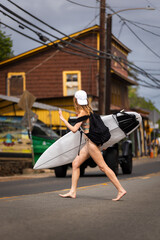 Surfer girl with a surfboard crossing road in hawaii surf town north shore