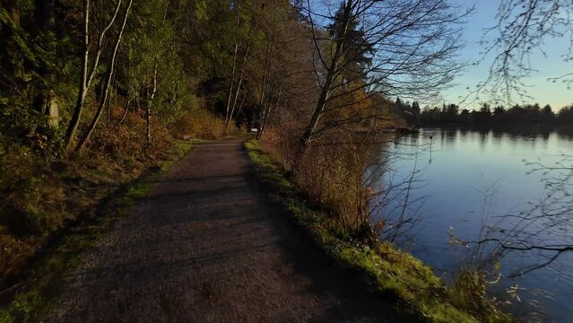 Path and View of Lost Lagoon. Famous Stanley Park. Sunny Fall Morning. Modern city with buildings skyline in background. Colorful Sunrise. Downtown Vancouver, British Columbia, Canada. Slow Motion