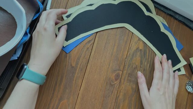 Female's hands lay out cloth and plastic base in form of ethnic Slavic crown on wooden table. Seamstress and her workplace. Headdress from eco-leather and adhesive woven interlining fabric.