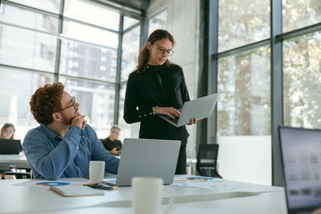 Two diverse business colleagues disscuss biz issue while use laptop in office background