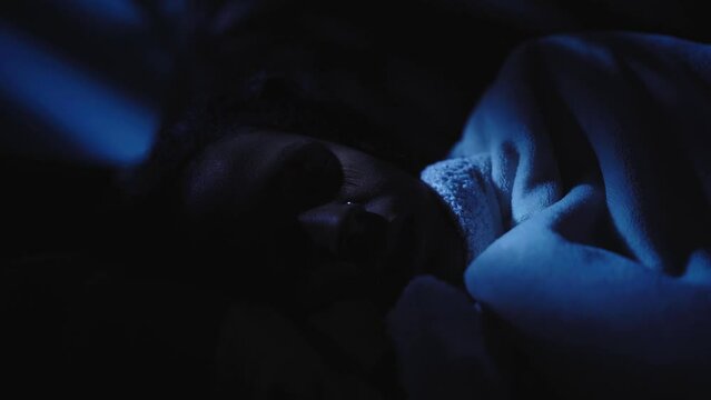 Close up of young black woman sleeping in bed at home in dark room. African American girl during comfortable nap resting in bedroom at night. Female people waking up in middle of evening indoors.