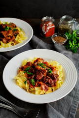 German Goulash Served Over Egg Noodles in Shallow Bowls: Simmered chunks of beef seasoned with marjoram, caraway seeds, and paprika
