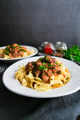 German Goulash Served Over Egg Noodles in a Shallow Bowl: Simmered chunks of beef seasoned with marjoram, caraway seeds, and paprika