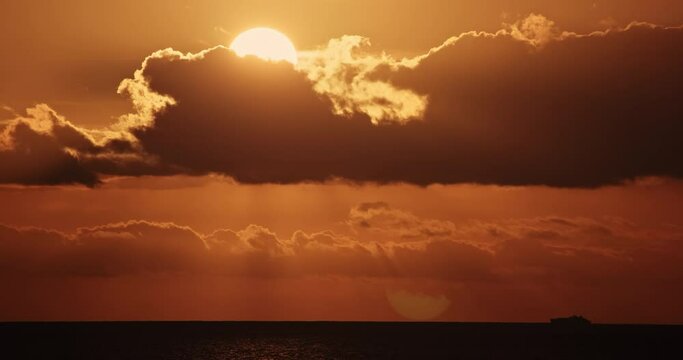 Sunset over the ocean time laps, extreme closeup sun setting down to sea water horizon, moving through clouds timelaps motion video, cinematic light rays, boat ship silhouette passing by nature 4K