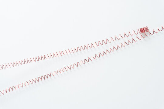threaded metallic wire spring or coiled stretched out across white paper background