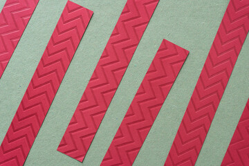 red paper stripes with embossed chevron or zig zag pattern on rough green paper