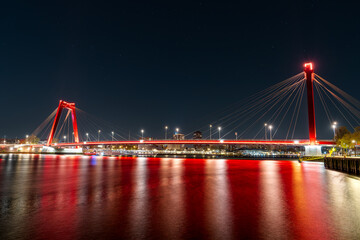 A stunning night view of the illuminated Willemsbrug Bridge in Rotterdam, Netherlands, with beautiful long exposure light trails creating a mesmerizing effect.