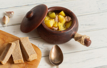 Roast in a ceramic pot with garlic and bread on a wooden light table