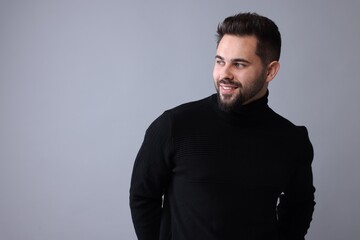 Obraz premium Happy man in stylish black sweater on grey background, space for text