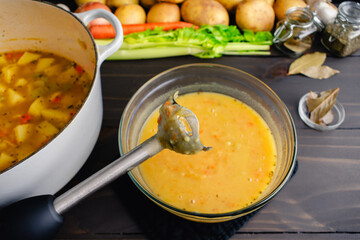 Close-Up of an Immersion Blender with Potato Soup in the Background: Stick blender used to blend...
