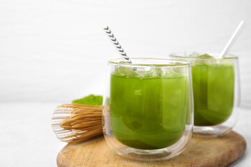 Delicious iced green matcha tea and bamboo whisk on white table, closeup. Space for text