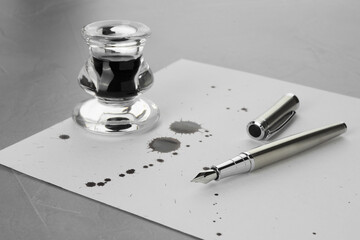 Stylish fountain pen, paper with drops of ink and inkwell on grey textured table