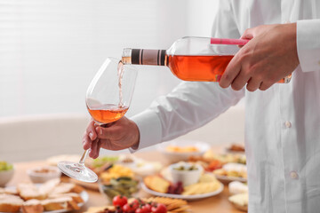 Man pouring rose wine from bottle into glass indoors, closeup