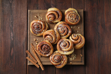 Tasty cinnamon rolls, sticks and nuts on wooden table, top view