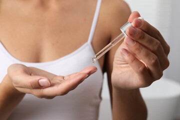 Woman applying cosmetic serum onto her finger on light background, closeup