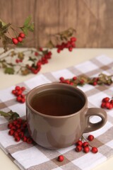 Brown cup with hawthorn tea and berries on beige table