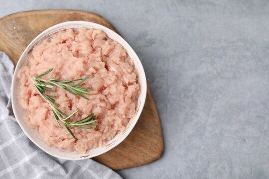 Fresh raw minced meat and rosemary in bowl on light grey textured table, top view. Space for text