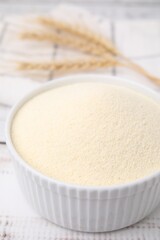 Uncooked organic semolina in bowl on white wooden table, closeup