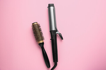 Hair styling appliance. Curling iron and round brush on pink background, top view