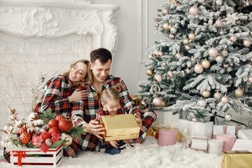 Mother, father and daughter sitting on s floor near Christmas tree