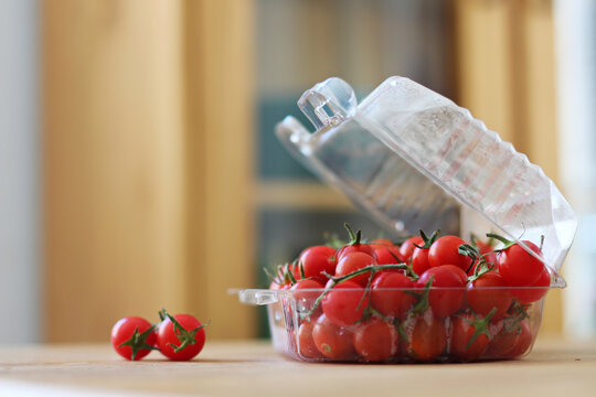 tomates cereja maduros dentro de recipiente plástico sob luz natural, sobre a mesa da cozinha em foco seletivo