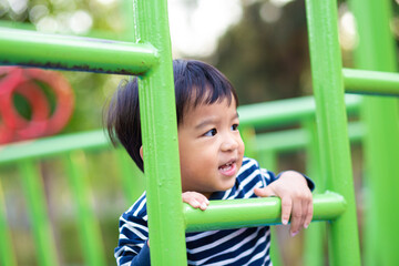Fototapeta premium Happy toddler asian 2 year boy climb on bar outdoor playground park