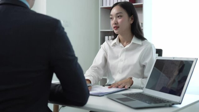 A successful businessman interviews a smart young woman for work in a respectful, professional atmosphere with a busy conversation. Two sides in modern office