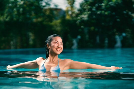 Young asian woman relaxing in the water, Beautiful girl relaxing at overwater infinity pool luxury resort. Spa, wellness, swimming.