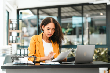 Attractive smiling African American female lawyer reads a document in an office, with a laptop, gavel, and scales of justice nearby, legal, legislation.